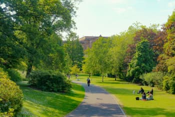 A picturesque park in Scotland with people enjoying a sunny day, surrounded by lush green trees.