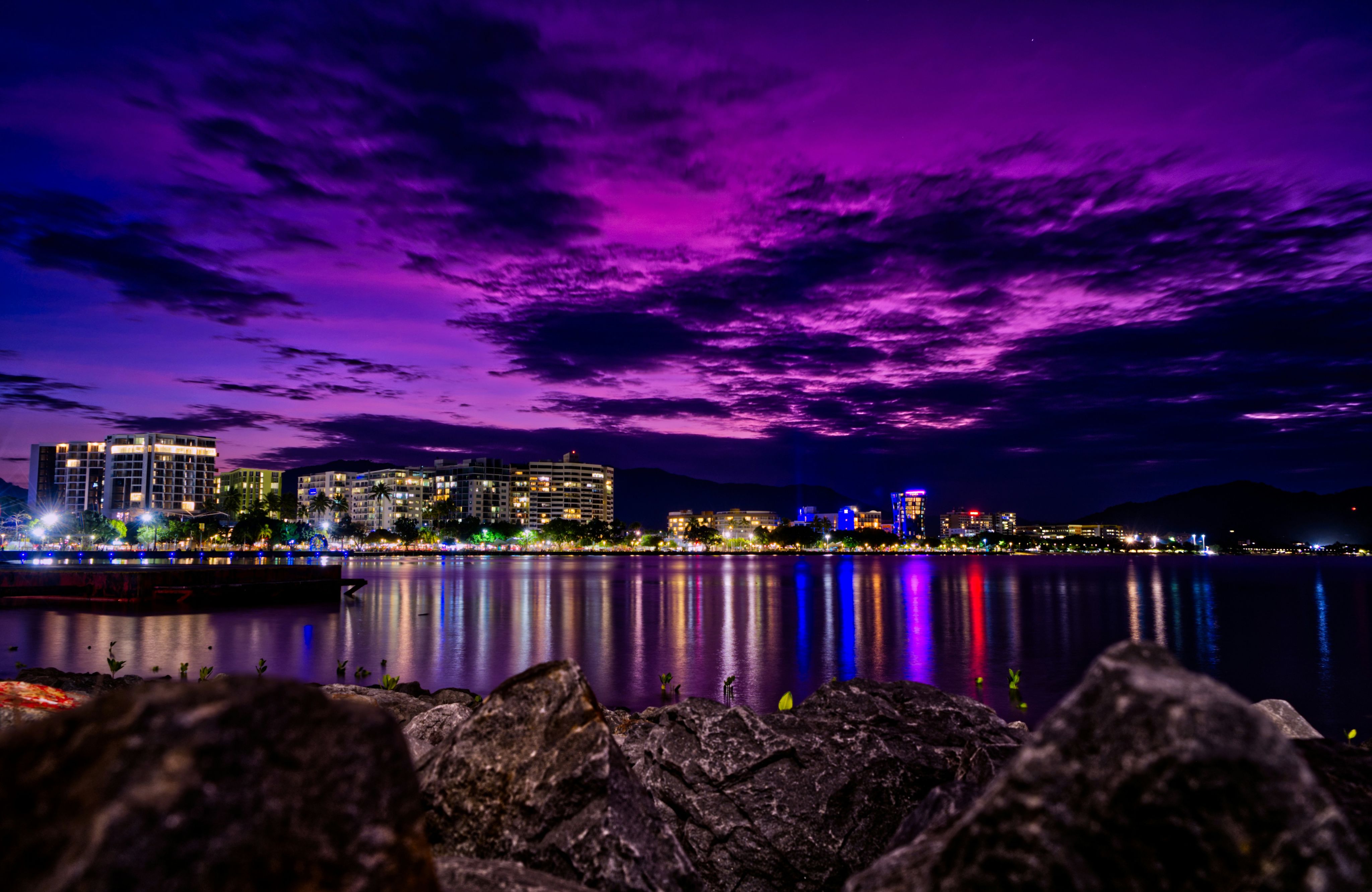 grey seashore rock with view of city skyline during night time