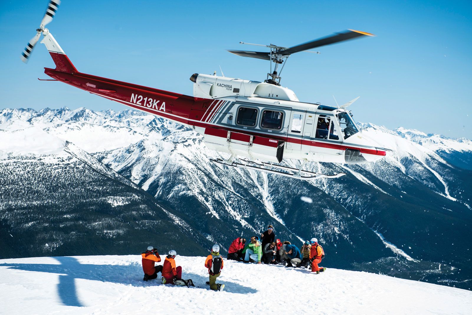 A CMH helicopter departs after depositing skiers atop a mountain peak.