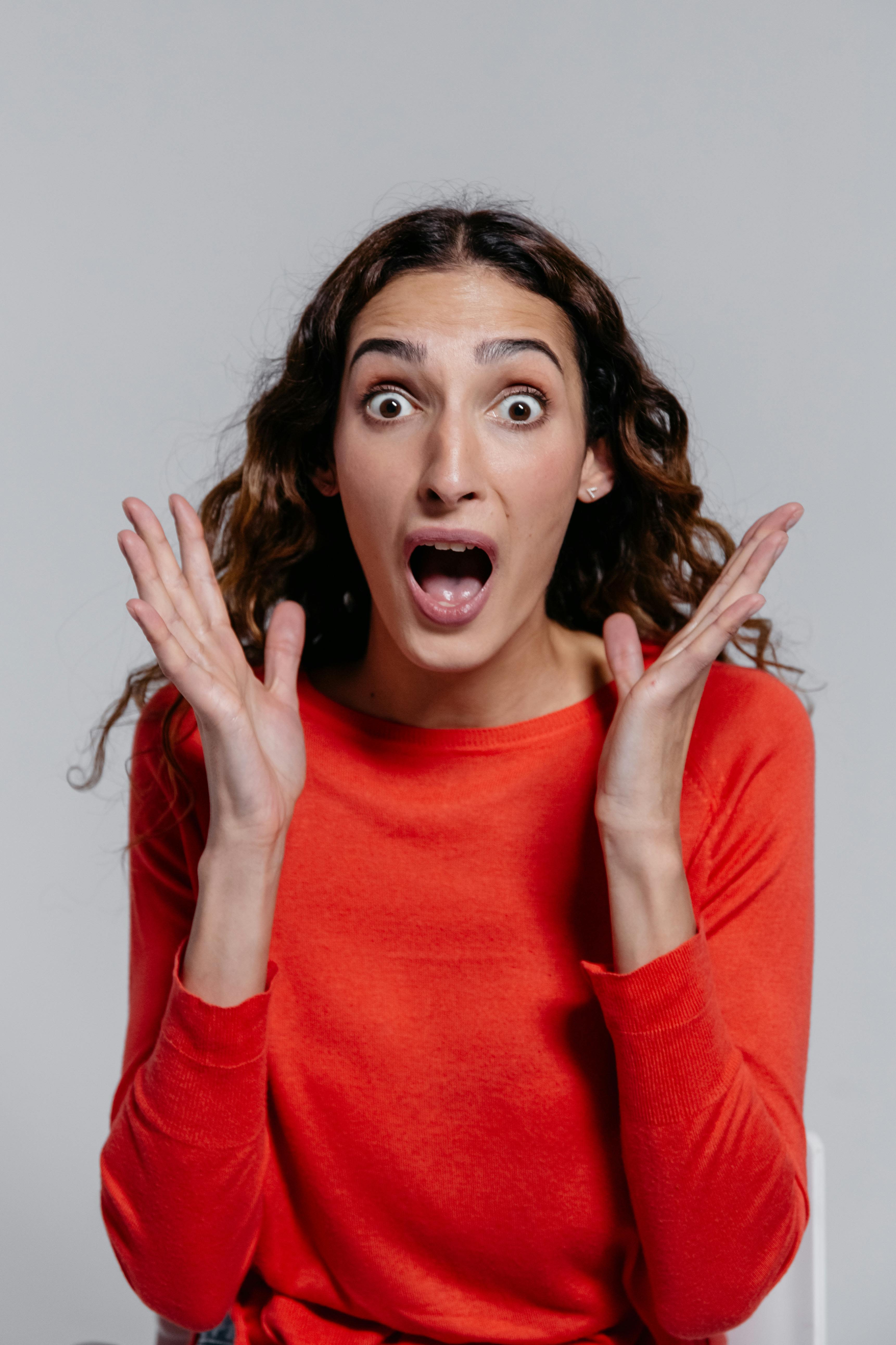 Portrait of a surprised woman with hands raised, showcasing a shocked facial expression.
