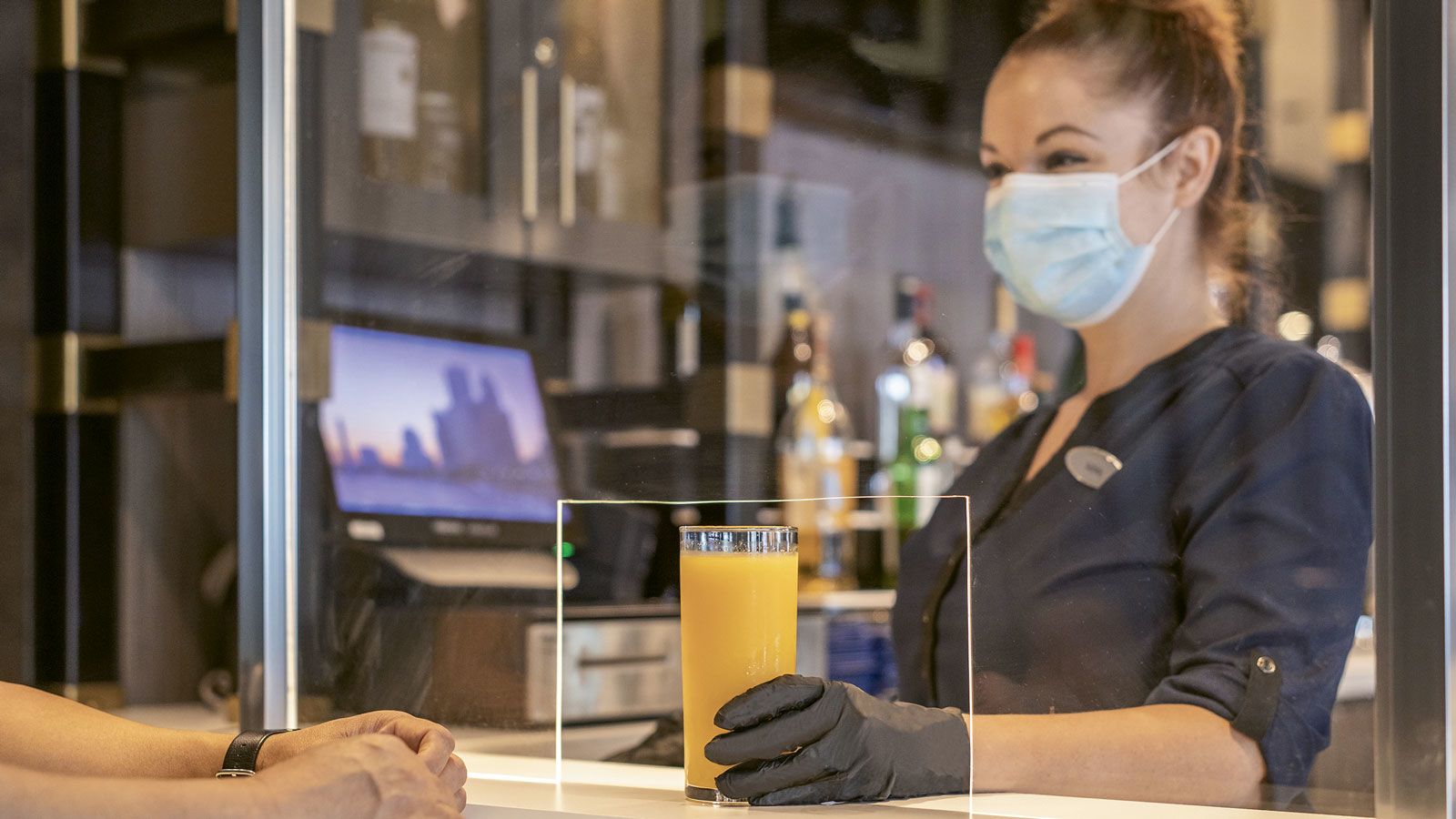 A bartender at a Hyatt hotel passes a drink through an opening in a glass partition.