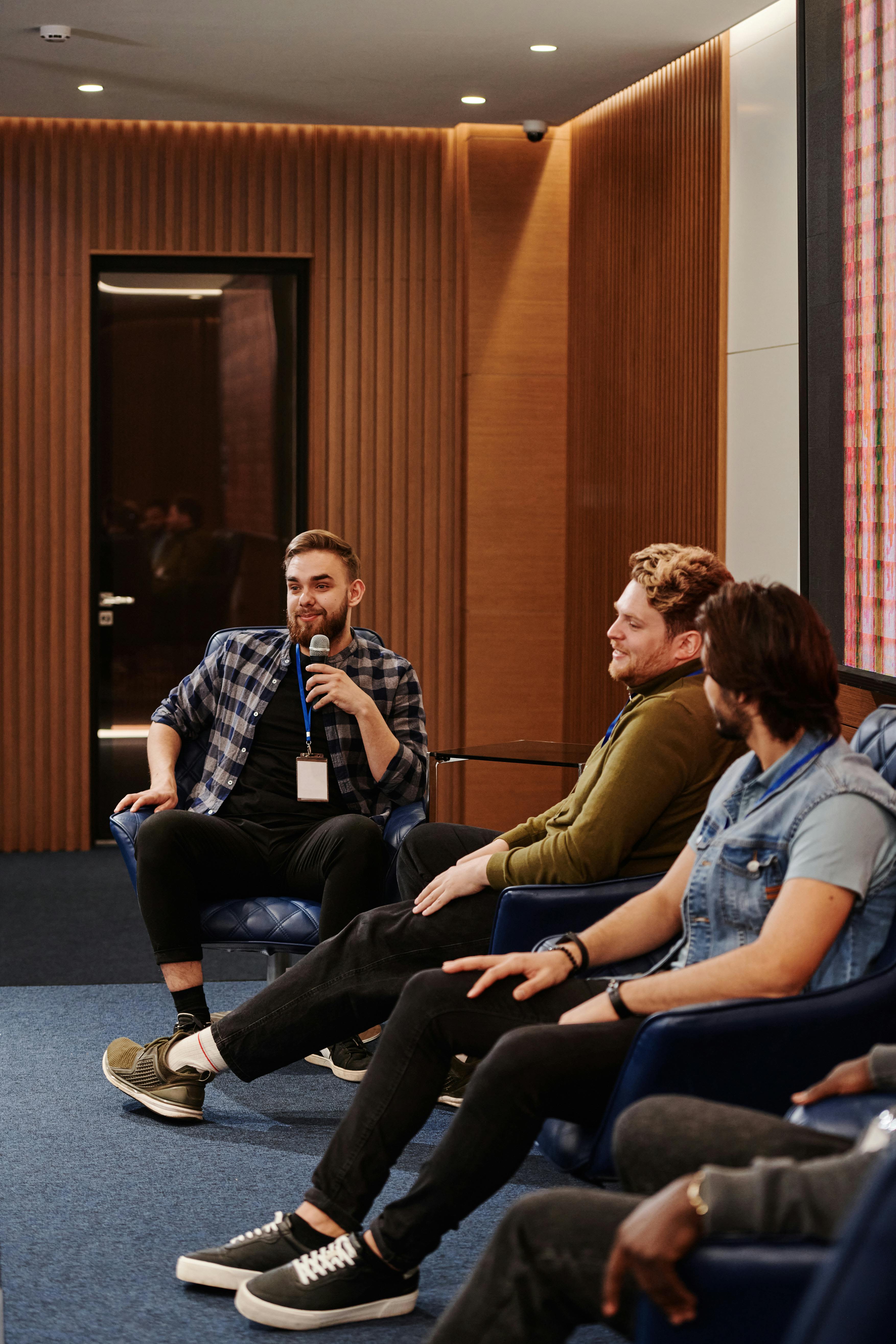Men engage in a relaxed conversation during an indoor panel discussion.