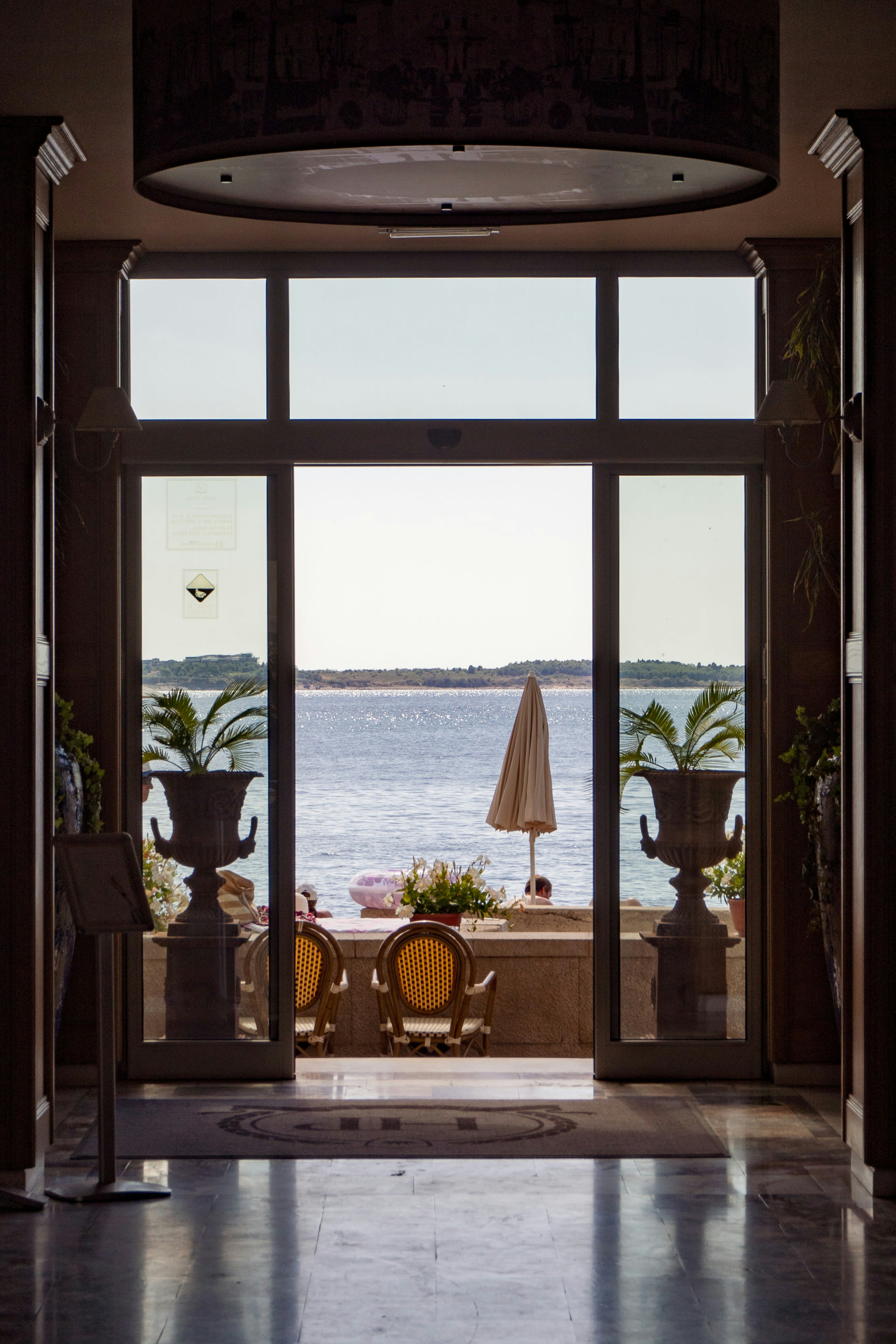 a patio with a table and chairs and a large window with a view of the ocean