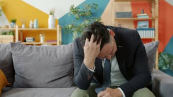 Man in suit sitting on couch with head in hands.