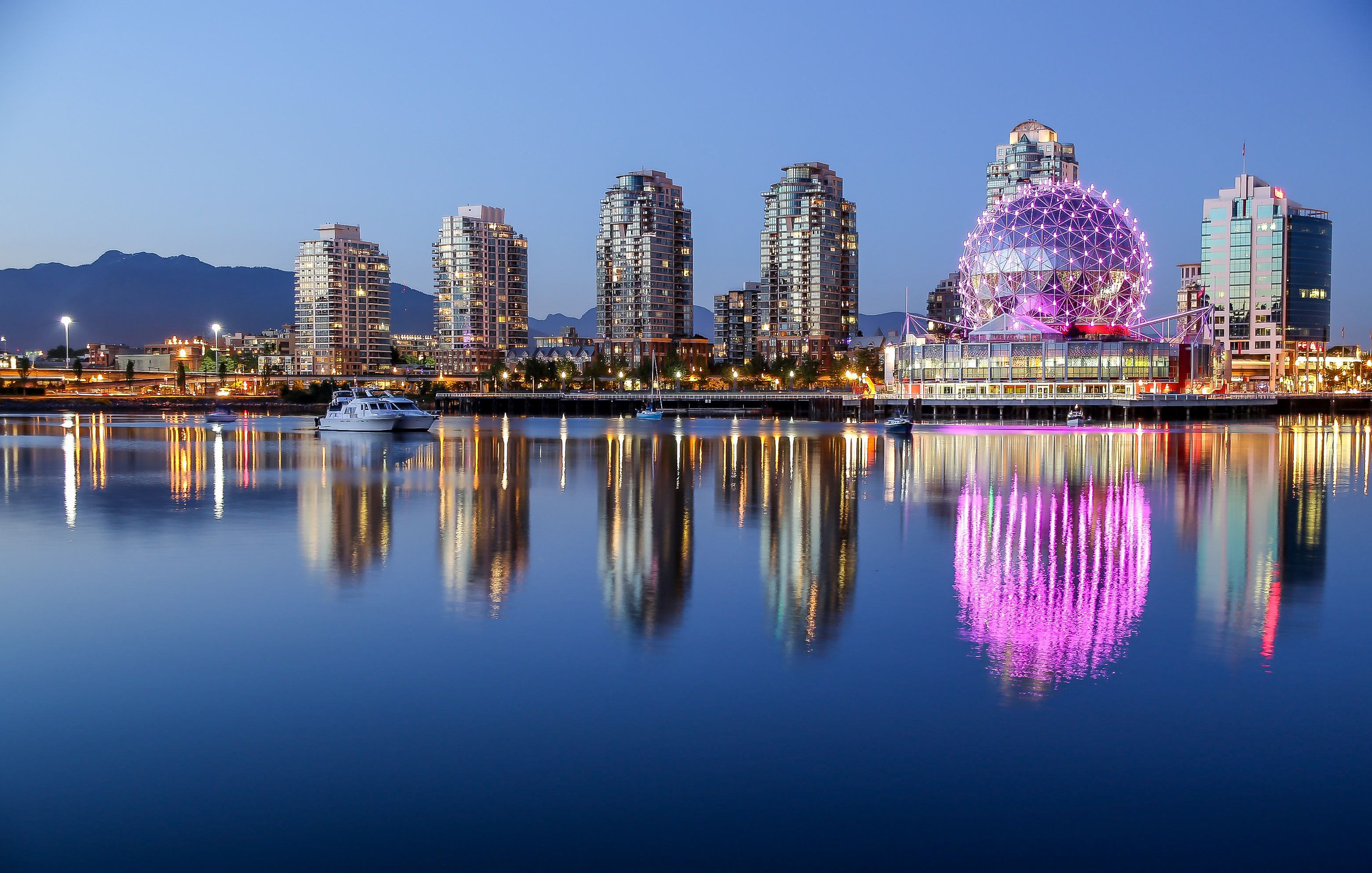 A beautiful clear summer night in Vancouver, BC features a pink glowing Science World  with reflections on the water at dusk