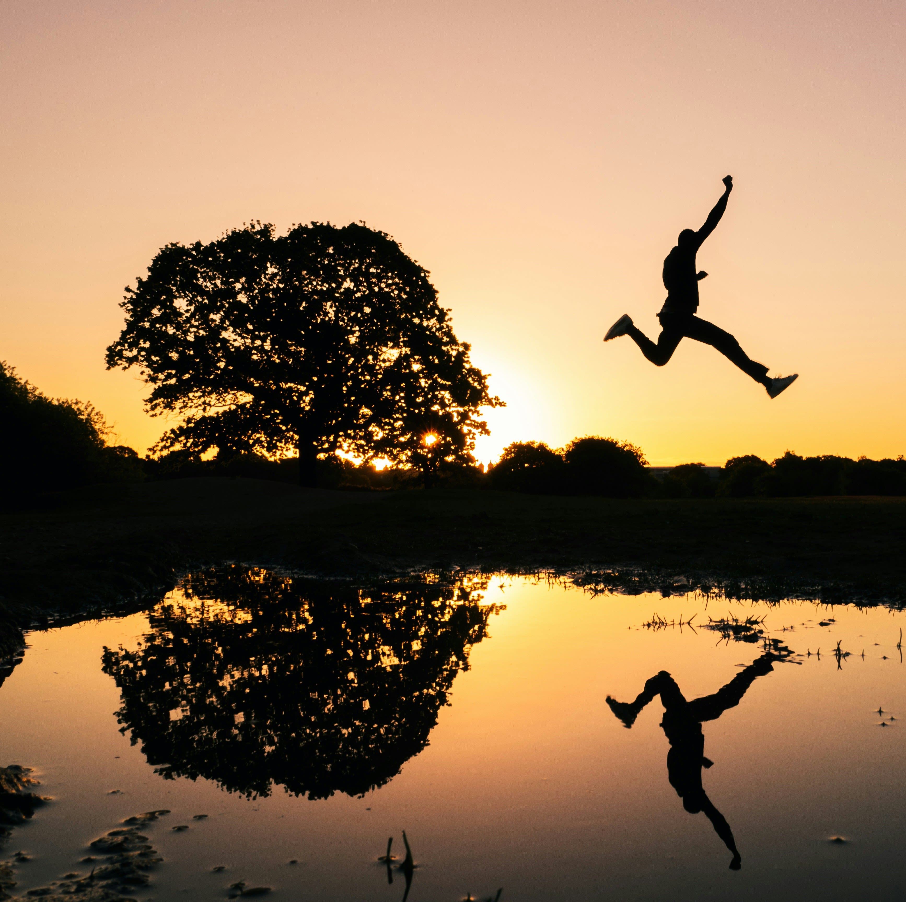 silhouette photo of man jumping on body of water during golden hour