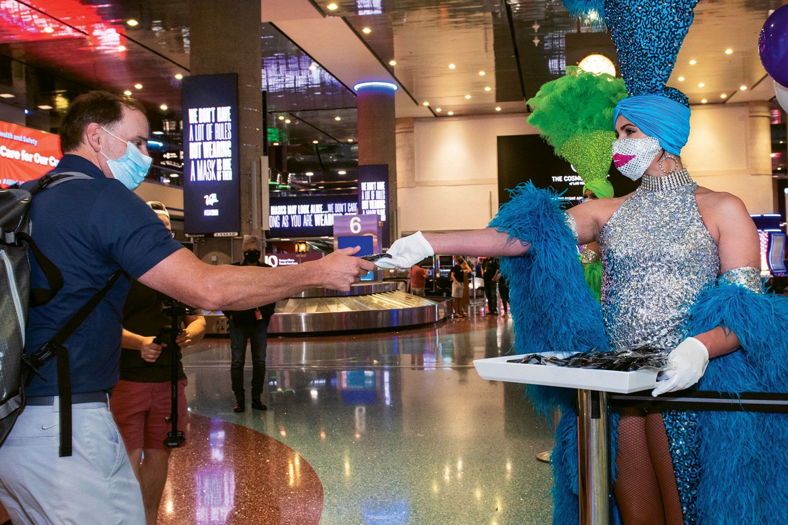 A Las Vegas showgirl hands an arriving visitor a mask at McCarran Airport.